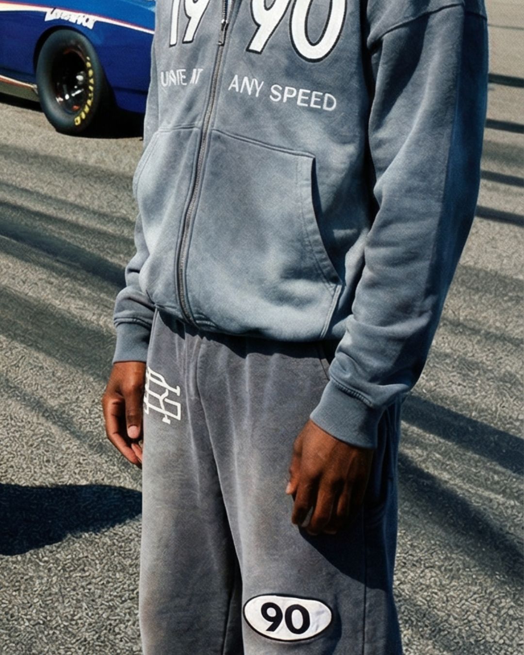Product shot of man wearing Grey 90 Sweatpants with SMALL AND RARE insignia on the top right thigh and "90" patch on the left mid-thigh featuring Grey 90 Zip Hoodie with "1990" and "Unsafe At Any Speed" on the chest.
