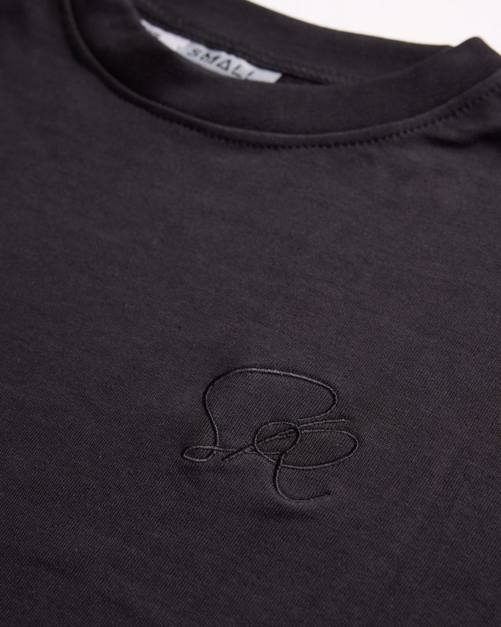Close-up of the Essential Black Crewneck Sweatshirt featuring black embroidered insignia on left chest.