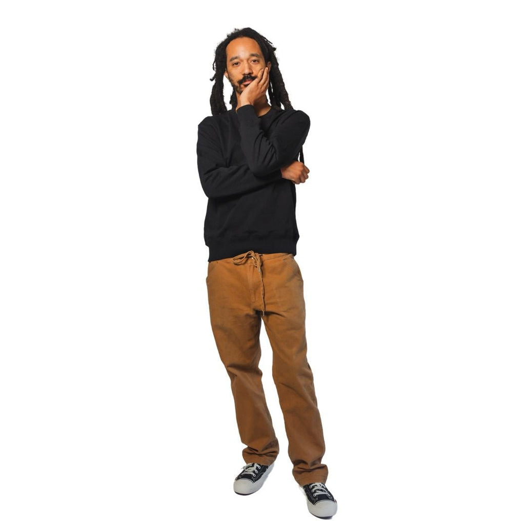Product shot of man wearing Essential Black Crewneck Sweatshirt featuring black embroidered insignia on left chest.
