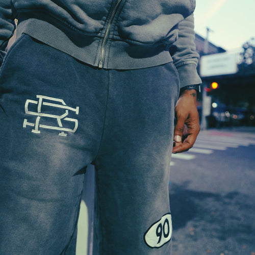 Clos-up product shot of a man wearing Grey 90 Sweatpants with SMALL AND RARE insignia on the top right thigh and "90" patch on the left mid-thigh featuring the Grey 90 Zip Hoodie.