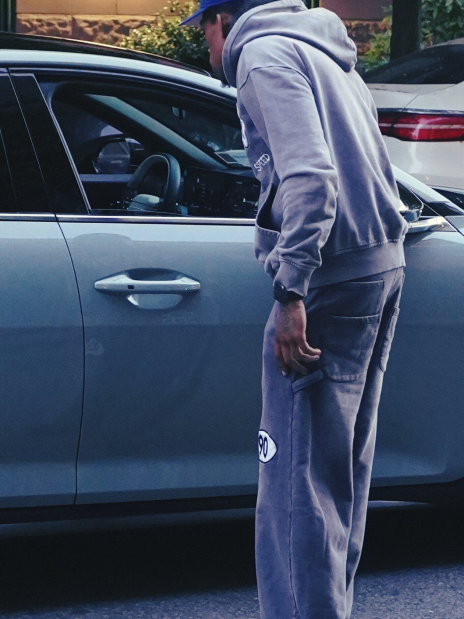 Person in Grey90 hoodie and pants standing next to a car.