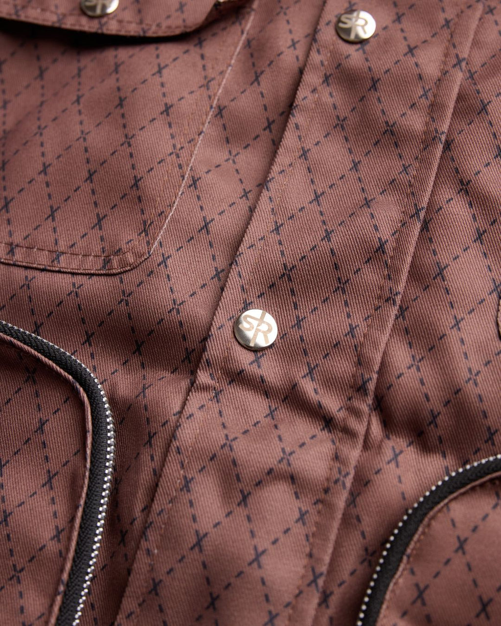 Close-up product shot of the Versa Workwear Jacket's silver embossed snap buttons and delicate textile pattern.