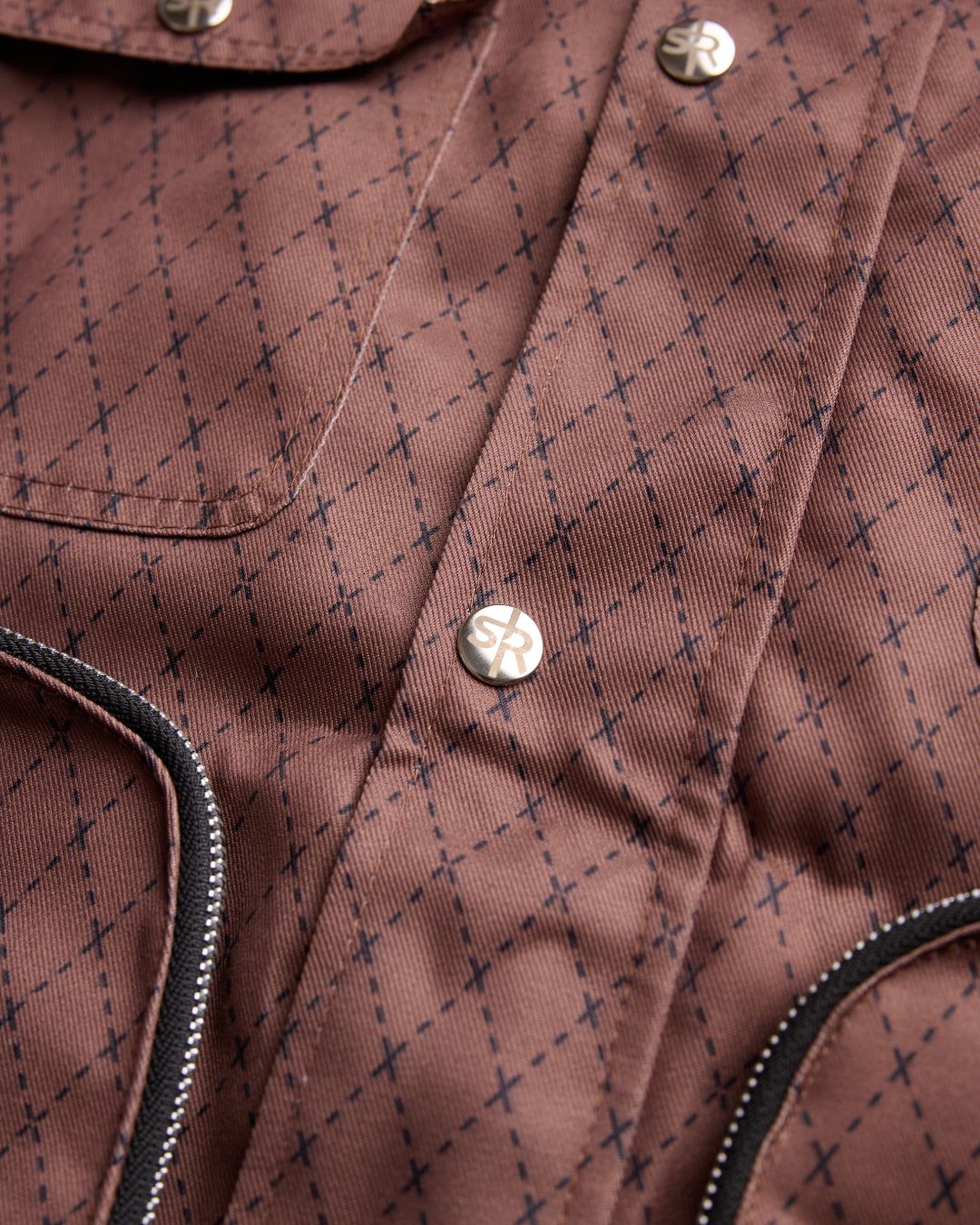 Close-up product shot of the Versa Workwear Jacket's silver embossed snap buttons and delicate textile pattern.